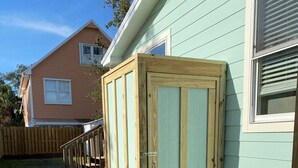 A wooden shed with a metal door, adjacent to a house with a light blue exterior.