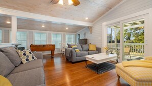 A spacious living room with a wooden ceiling, a gray sofa, a white coffee table, and a yellow ottoman.