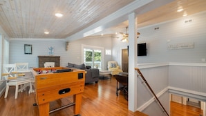 A spacious living area with a foosball table, a television, and a cozy seating area with a sofa and chairs.