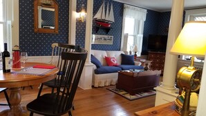 Un salon avec une table ronde en bois, une chaise noire, un canapé avec des coussins bleus, un petit tapis et une lampe.
