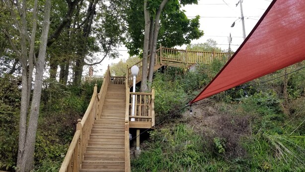Un escalier en bois menant au sommet d’une colline, entouré d’arbres et de végétation.