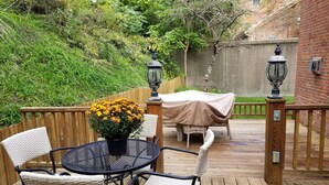 Une terrasse en bois avec une table ronde et quatre chaises, une table abritée avec un banc, et deux lampes de style lanterne.