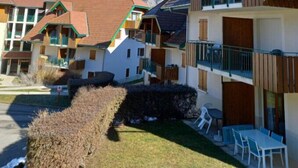 A row of chalet-style buildings with balconies, a clear view of snow-capped mountains in the background, and a well-maintained lawn in the foreground.