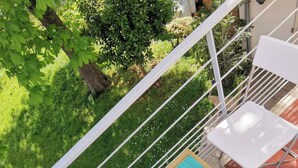 Une terrasse avec une table dressée pour deux personnes, entourée de chaises blanches, et une vue sur le jardin.