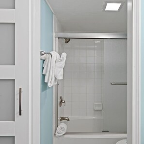 Ein Badezimmer mit Duschkabine aus Glas, weißen Fliesen und einem Handtuchhalter mit Handtüchern.