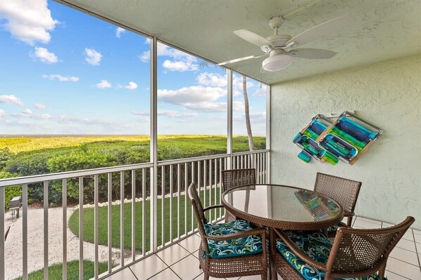 A balcony with a glass table and wicker chairs, overlooking a green landscape.