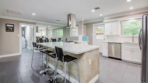 A modern kitchen with a central island, bar stools, stainless steel appliances, and a view to the outdoors.