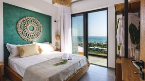 Une chambre moderne avec un grand lit, une décoration murale, une vue sur l’océan et un balcon où du linge est étendu.