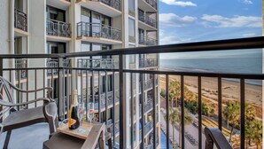Un balcon avec vue sur la plage, une bouteille de champagne et un verre posé sur une table.