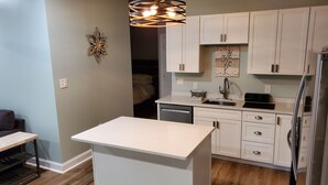 Een moderne keuken met witte kasten, een centraal eiland, een geïntegreerde vaatwasser en een hanglamp.