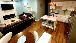 Een knus woongedeelte met een bank, een eettafel met stoelen, een keuken met witte kasten en een flatscreen televisie aan de muur.