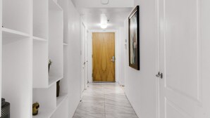 A hallway with white walls, a wooden door at the end, and white shelving units along the sides.
