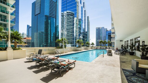 A rooftop pool area with lounge chairs, a swimming pool, and a view of tall buildings.