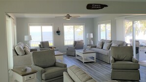 A spacious living room with a large window overlooking a body of water, a ceiling fan, and a sign with coordinates. - Waterfront Paradise on the Eastern Shore of Chesapeake Bay  (Rock Hall)