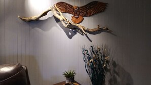 Quarto com escultura de madeira de uma águia, uma poltrona de couro e uma pequena planta em vaso.