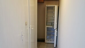 Ein schmaler Korridor mit einer weißen Tür, einem Kühlschrank und Holzschränken.