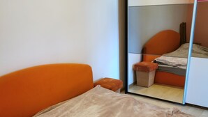 Ein Schlafzimmer mit einem Bett, das mit einer beigen Decke bezogen ist, einem orangefarbenen Kopfteil und einem kleinen, orangefarbenen Hocker.