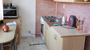 Eine kompakte Küche mit Backstein-Spritzschutz, einem Gasherd, einer Spüle und einer kleinen Essecke mit Tisch und Stühlen.