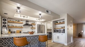 A modern kitchen with a central island, bar stools, a refrigerator, microwave, and a stove. - 4BR Townhome | Pool | Old Town Scottsdale (Scottsdale)