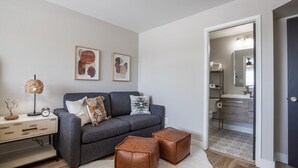 A modern living room with a grey sofa, two leather poufs, a white rug, and a desk with a lamp and decorative items. - 4BR Townhome | Pool | Old Town Scottsdale (Scottsdale)