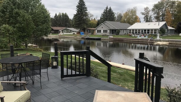 Terraza con mobiliario exterior, vista a un lago y casas circundantes.