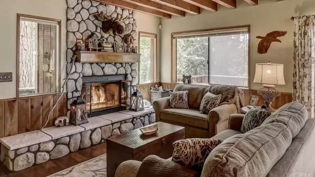 A cozy living room with a stone fireplace, wooden beams, a sofa set, and a large window. - Lake Home in the Pines with a Dodger history (Lake Arrowhead)