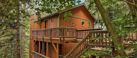 Une cabane en bois dotée d’un balcon et d’un escalier, entourée d’arbres.
