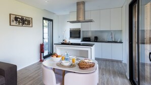 A modern kitchen with white cabinets, a built-in oven, and a microwave. There is a dining table with chairs and a fruit bowl. - Vila Vicente-Wellness, Fantastic Views and Parking (S. Vicente Ferreira)