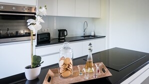 A modern kitchen with a black countertop, a stainless steel oven, white cabinets, a coffee maker, a sink, and a decorative tray with cookies and glasses. - Vila Vicente-Wellness, Fantastic Views and Parking (S. Vicente Ferreira)