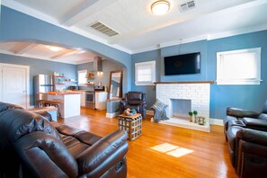 A living room with a fireplace, a television mounted above it, and a kitchen in the background. - Beautiful bungalow located in the heart of El Paso (El Paso)