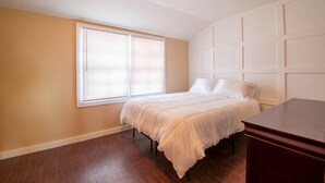 Un dormitorio con cama, ventana con persianas, suelo de madera y cómoda.