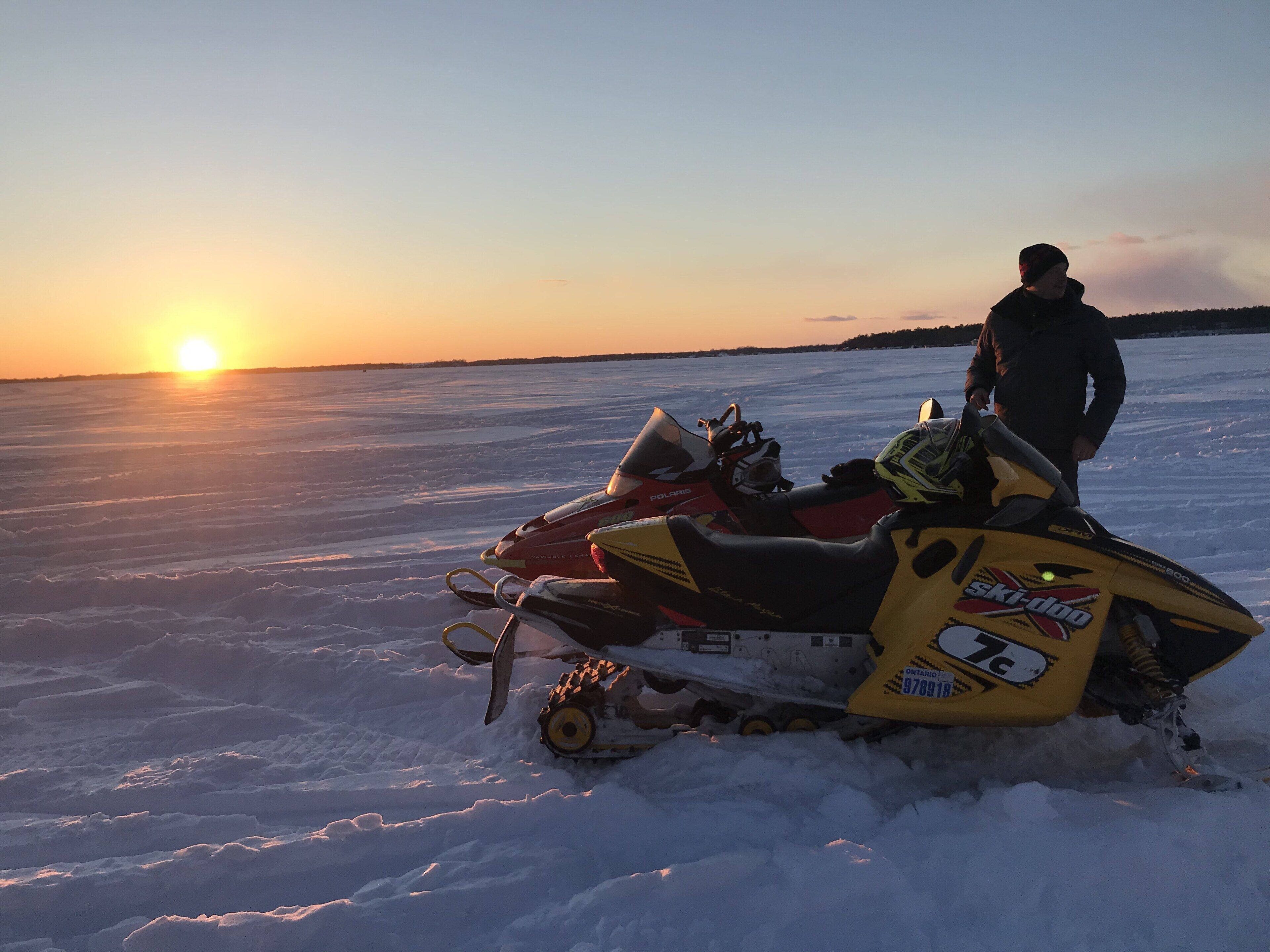 A snowmobile on a frozen lake with a person standing beside it.