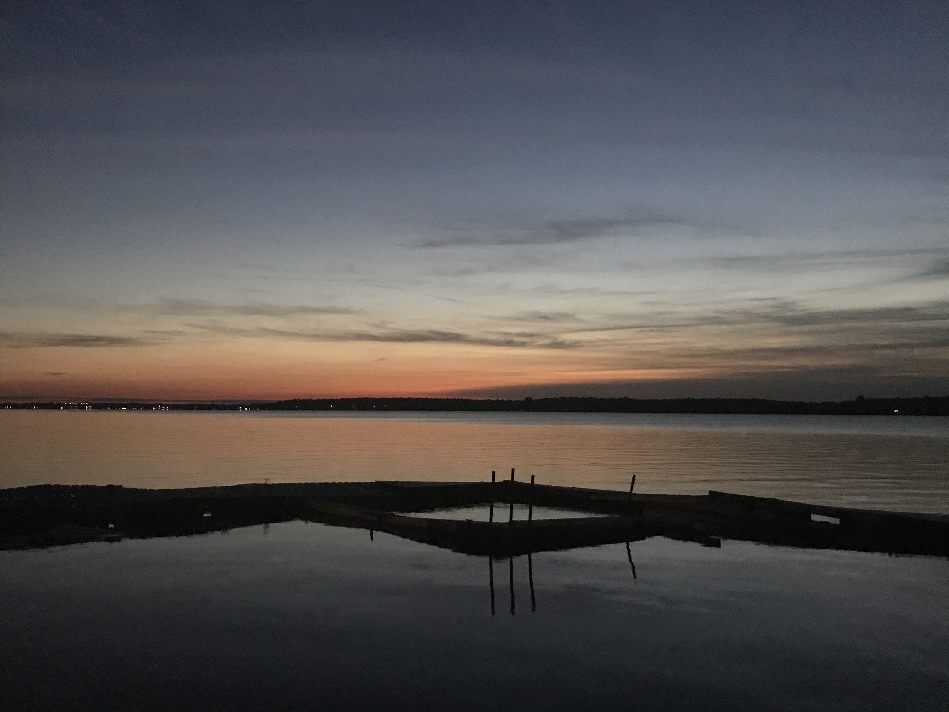 A calm waterfront at dusk with a dock extending into the water.