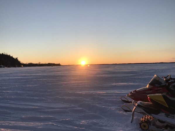 Un vehículo de nieve sobre un lago congelado, con el sol poniéndose al fondo.