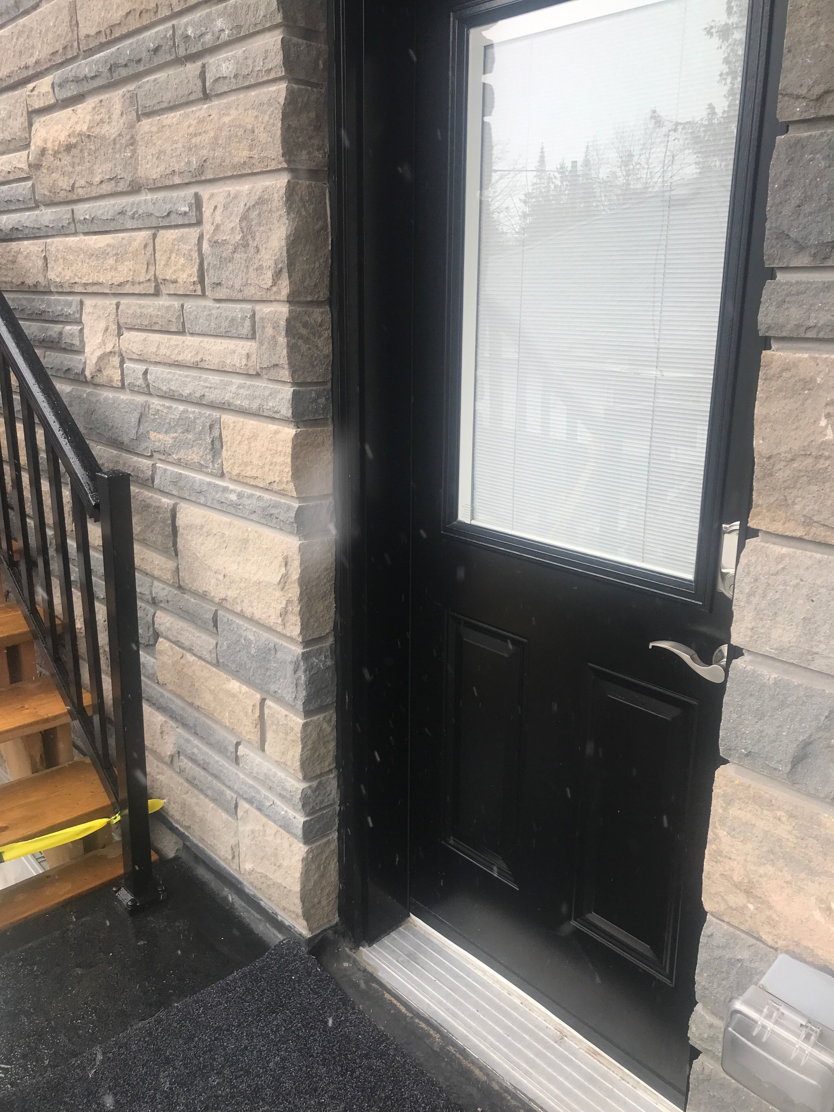 A stone exterior wall with a black door and a window.