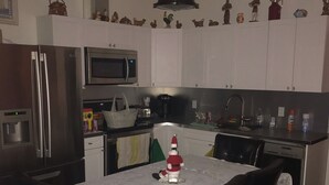 A compact kitchen with white cabinets, a stainless steel refrigerator, a microwave, and a coffee maker. There is a dining table with a lace tablecloth and four chairs.