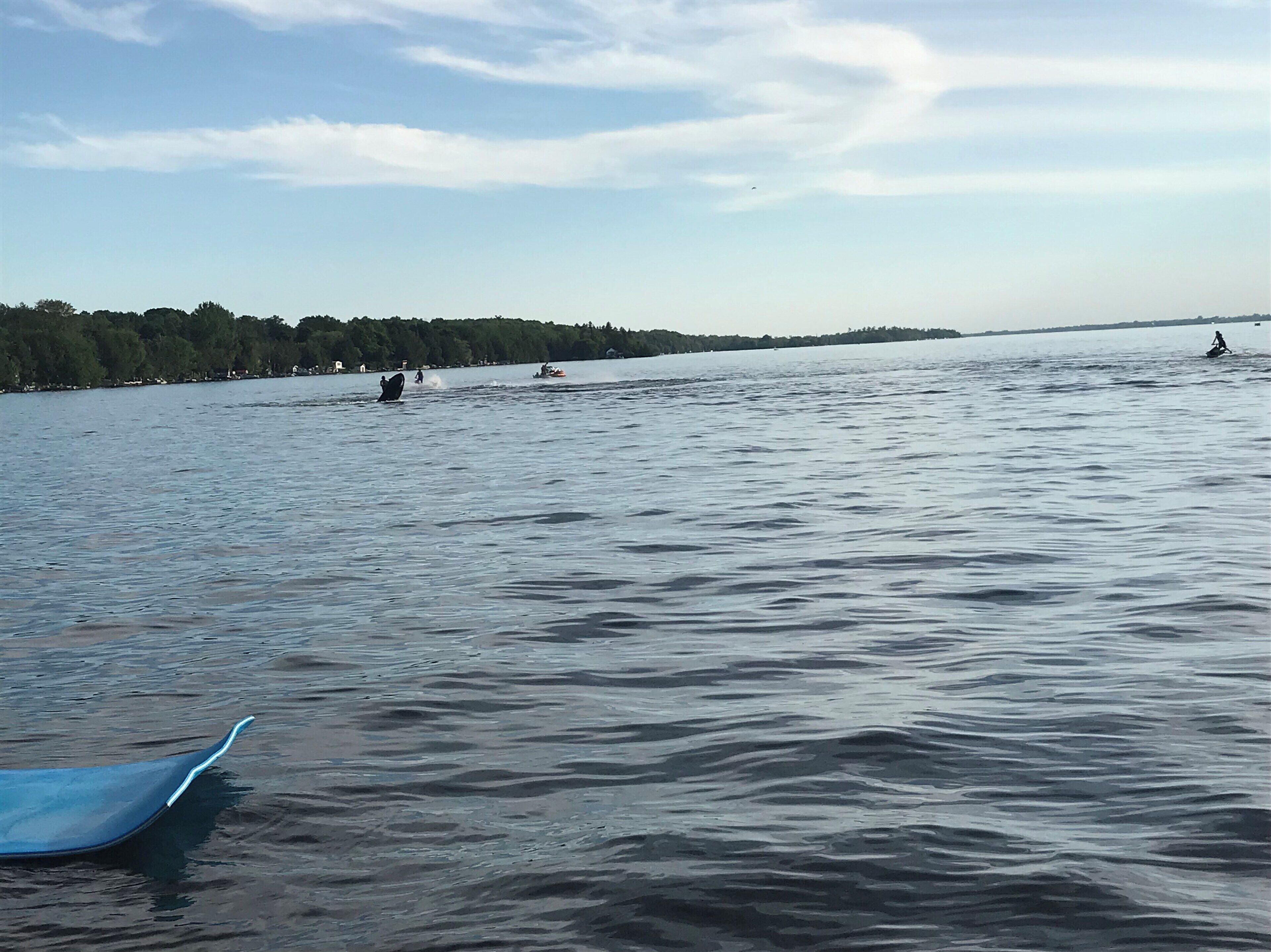 A calm lake with a boat in the foreground and a person on a jet ski in the distance.
