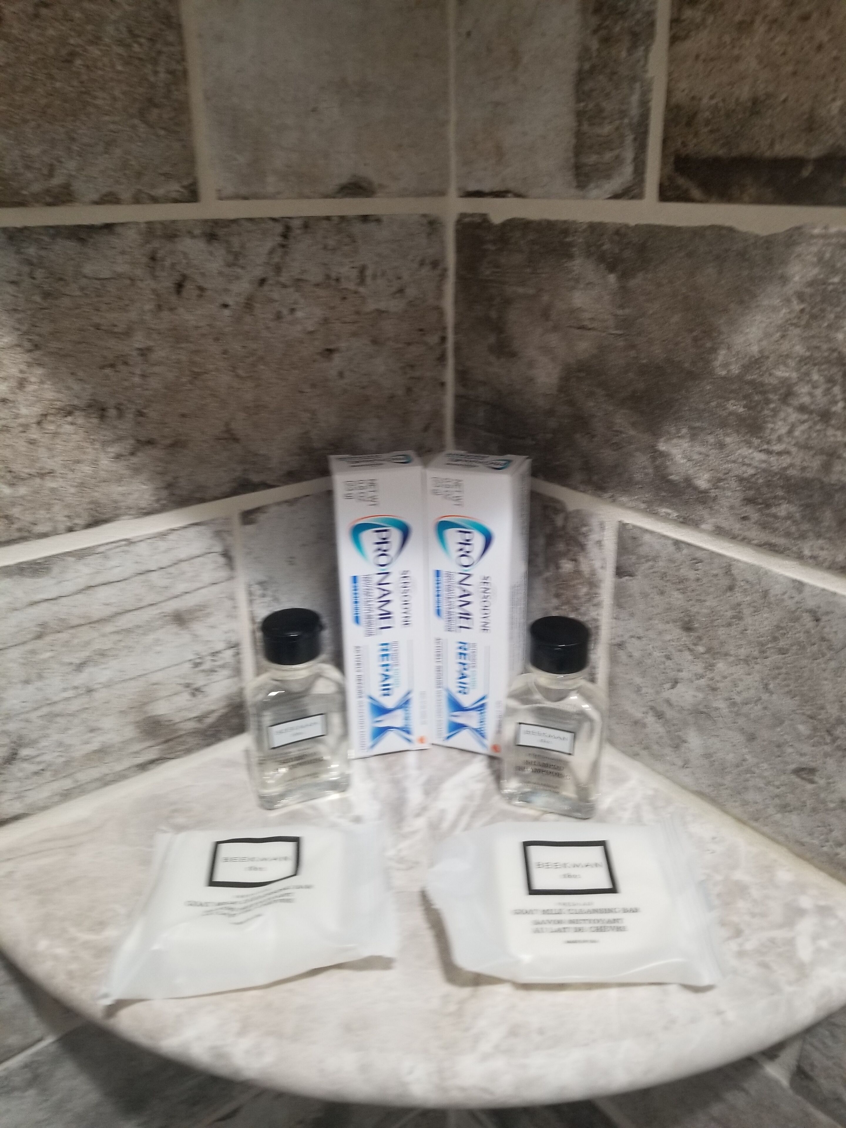 Une salle de bain avec un lavabo en marbre, deux flacons de savon pour les mains et deux boîtes de shampoing.