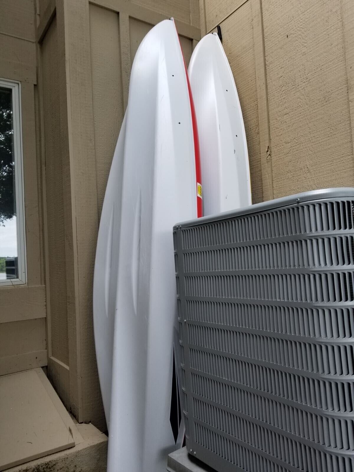 Two white surfboards leaning against a beige wall, with a metal grill in the foreground.