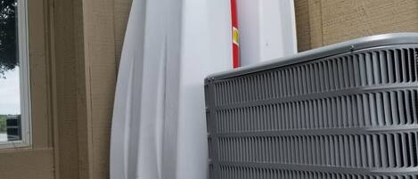 Two white surfboards leaning against a beige wall, with a metal grill in the foreground.