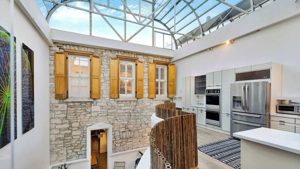 A spacious interior with a high ceiling, stone walls, wooden shutters, and a modern kitchen. - 6th St Mansion w Indoor Pool + Walk to Everything (Austin)