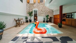 A swimming pool with a flamingo float, surrounded by potted plants and wooden furniture. - 6th St Mansion w Indoor Pool + Walk to Everything (Austin)