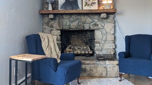 A cozy living room with a stone fireplace, two blue armchairs, a small wooden table, and a decorative vase. - Big Views, Hot Tub, Dog Friendly, 5min to BR (Blowing Rock)