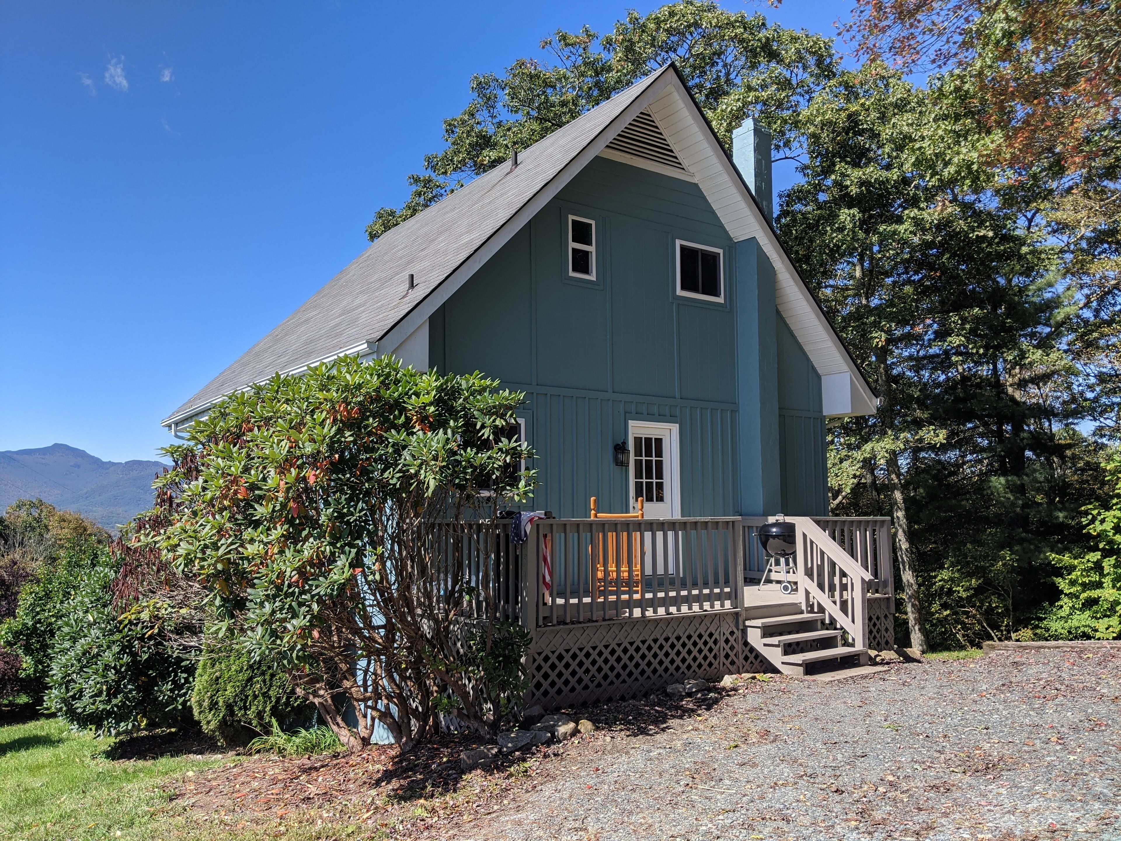 A two-story house with a porch, a small front yard, and a mountain backdrop.