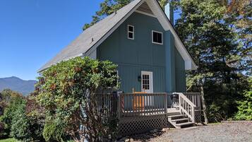 A two-story house with a porch, a small front yard, and a mountain backdrop.