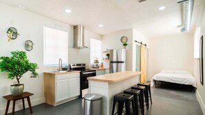 A modern kitchen with white cabinets, a stainless steel refrigerator, and a central island with stools. - Quaint cozy studio located in the heart of El Paso  (El Paso)