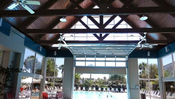 Uma piscina interior com vista desobstruída para o exterior, estrutura de cobertura e espreguiçadeiras ao redor da área da piscina.