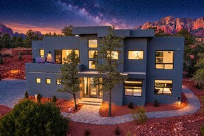 A modern two-story house with multiple windows, a paved driveway, and a starry night sky.