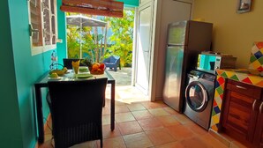 A compact kitchen with a washing machine, a refrigerator, and a dining area with a table and chairs. - T1 D'ALICE CLASS 2* 1.2 KM FROM BOURG BEACH (SAINTE ANNE)