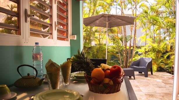 A dining table with plates, cutlery, a water bottle, and a fruit basket. - T1 D'ALICE CLASS 2* 1.2 KM FROM BOURG BEACH (SAINTE ANNE)